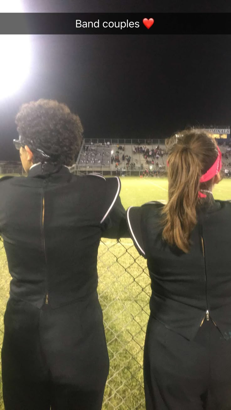 two women in black uniforms standing next to each other on a baseball field at night