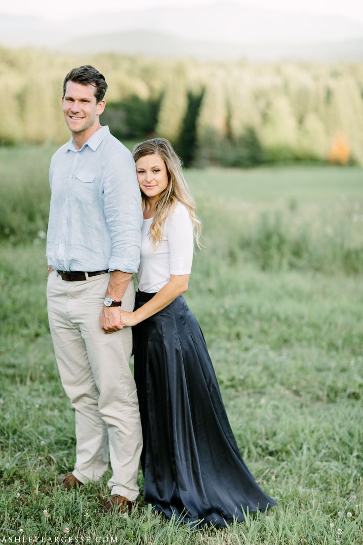 an engaged couple standing together in the grass