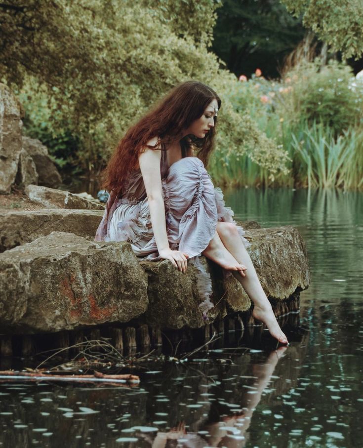 a woman sitting on top of a rock next to a body of water