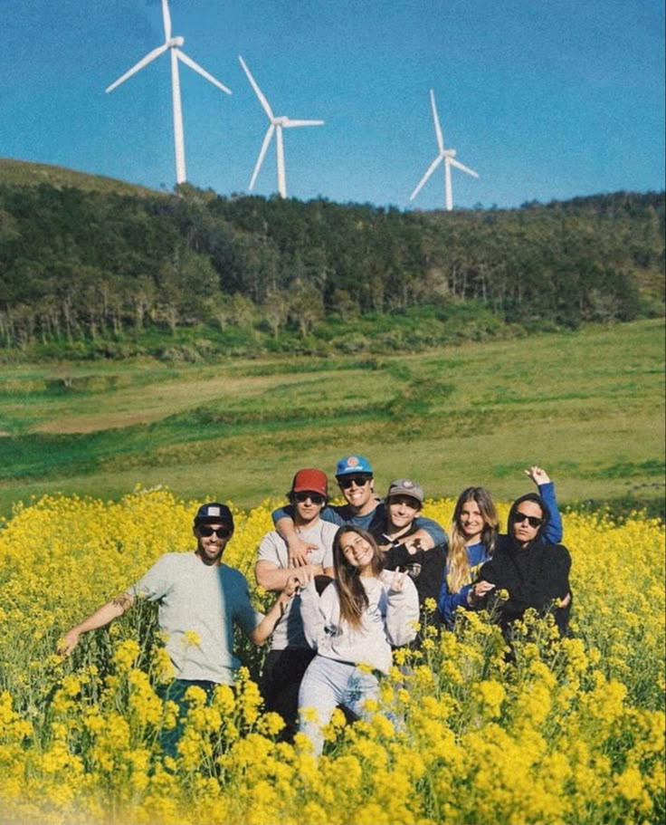 a group of people standing in a field with yellow flowers and wind mills behind them