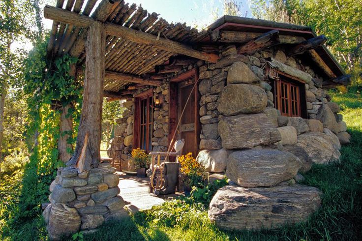 an old stone house with wood shinnings on the roof and windows is surrounded by large rocks