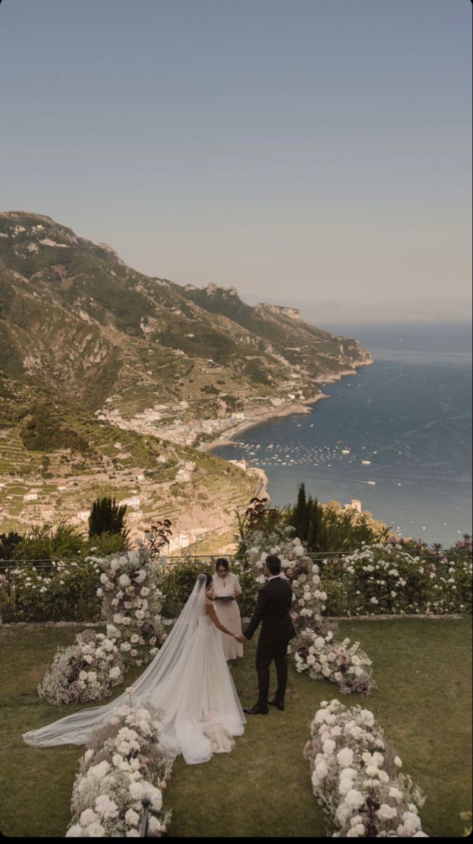 a bride and groom standing in front of the ocean at their wedding ceremony on top of a hill