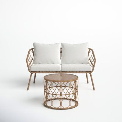 a wicker couch and coffee table with white pillows on it in front of a plain background