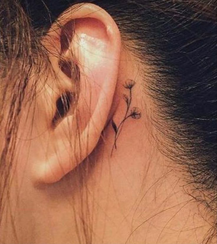 a woman's ear has a small flower tattoo on it