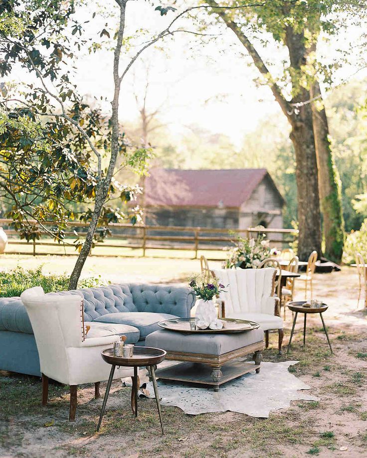 an outdoor seating area with couches, tables and chairs in front of some trees