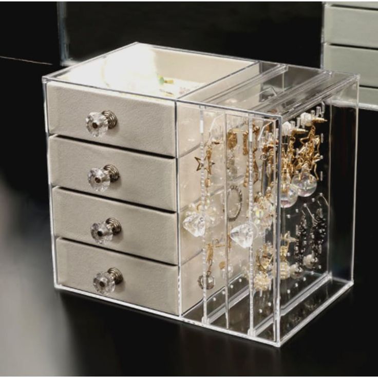 a clear jewelry box sitting on top of a wooden table next to a mirror and drawers