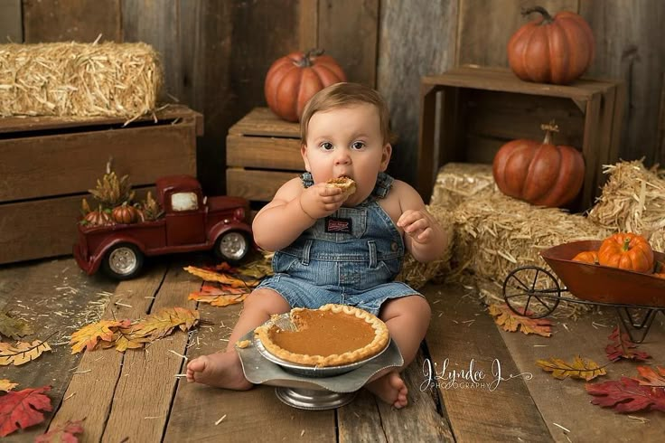 a baby sitting on the floor eating a piece of pie in front of pumpkins