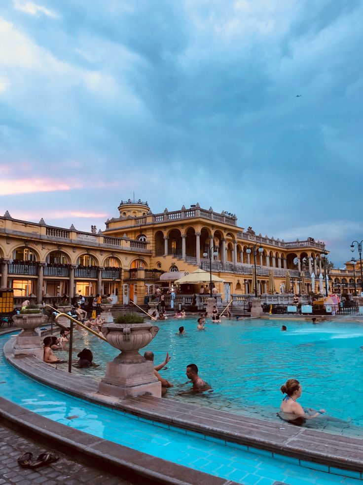 people are swimming in an outdoor pool at dusk