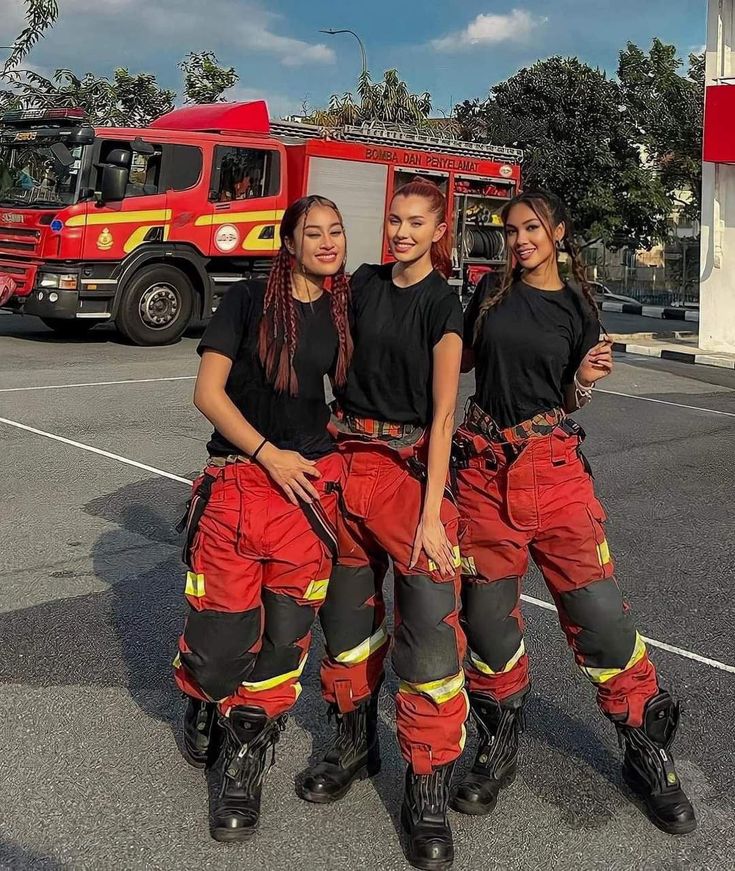 three women in red and black firefighter gear standing next to a firetruck