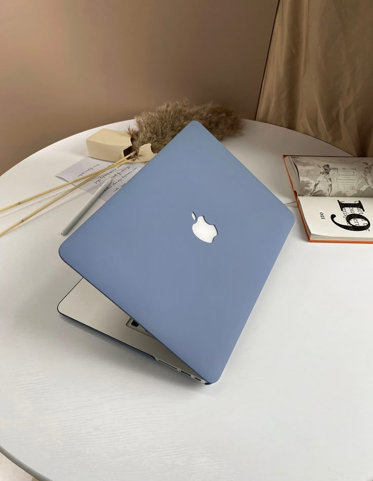 an apple laptop sitting on top of a white table next to books and a stuffed animal