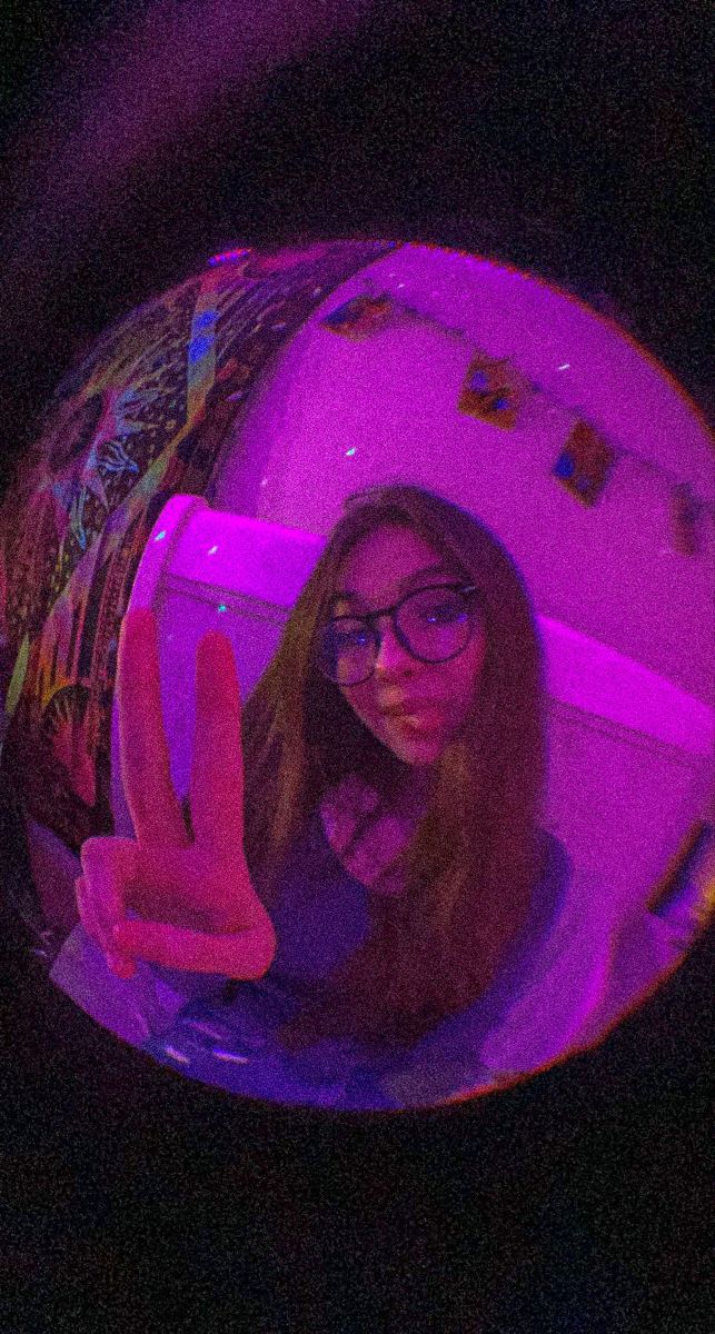 a woman with glasses is taking a selfie in front of a mirror that has purple light on it