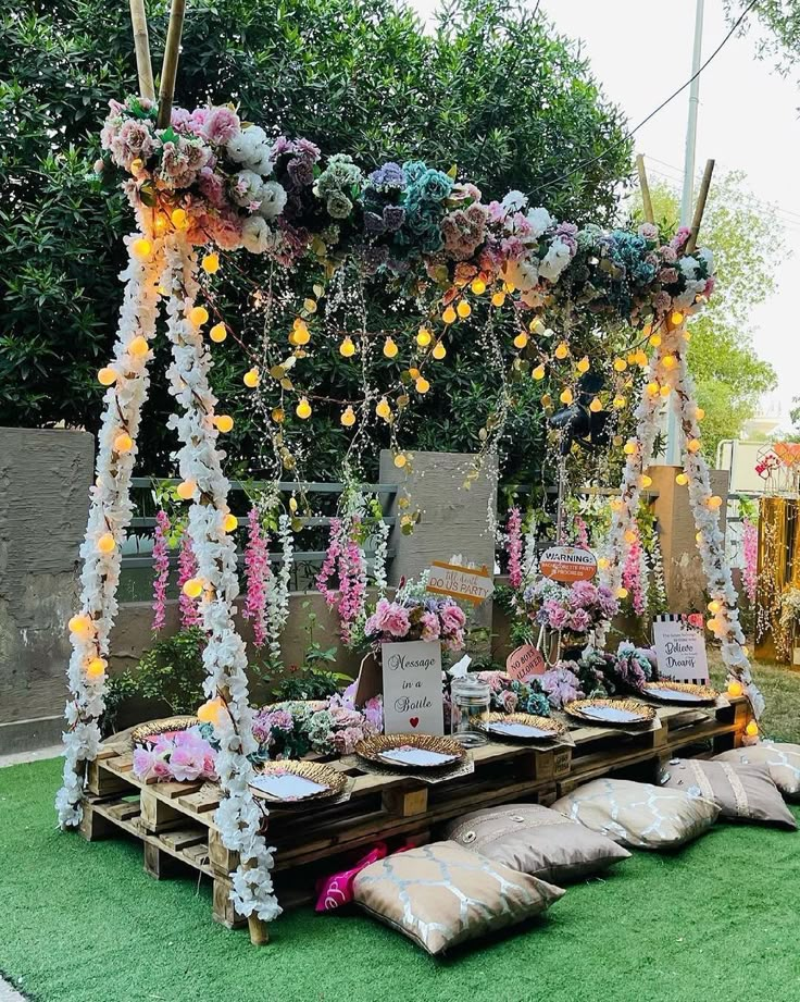 an outdoor wedding setup with flowers and pillows on the grass, surrounded by wooden pallets