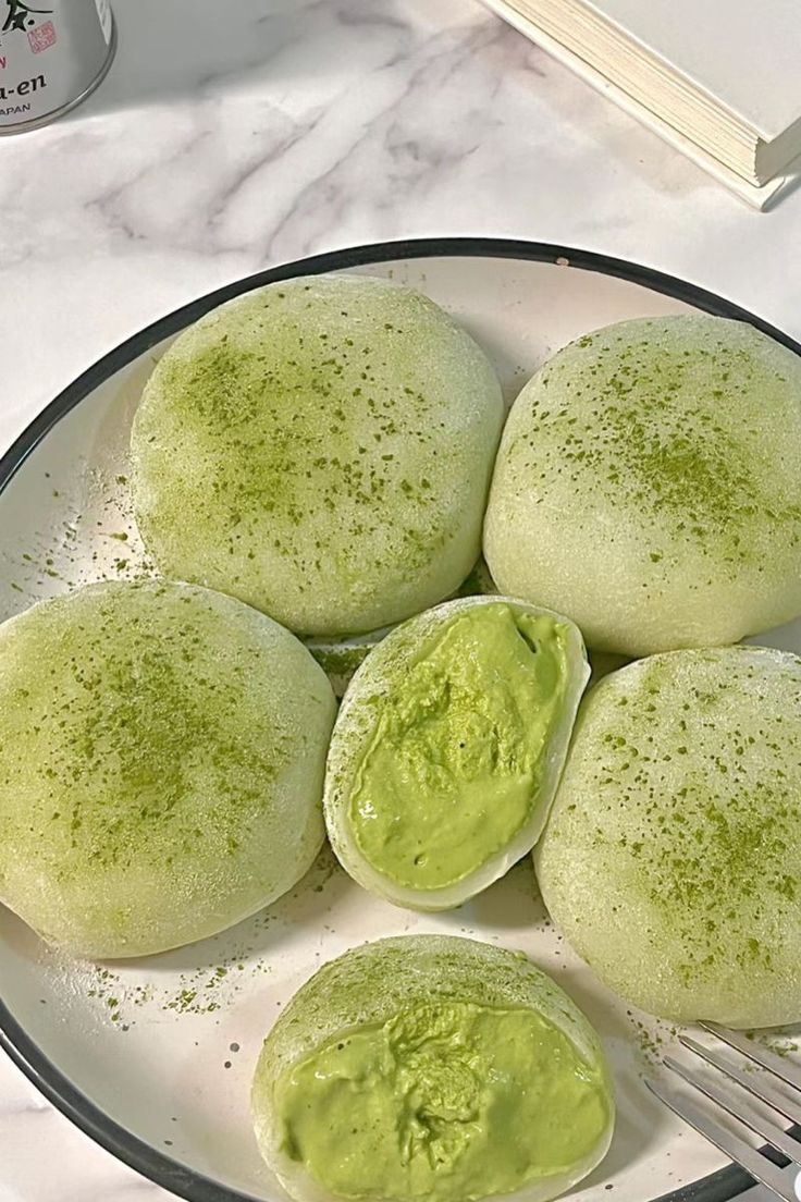 four green pancakes on a plate with a fork next to it and a book in the background