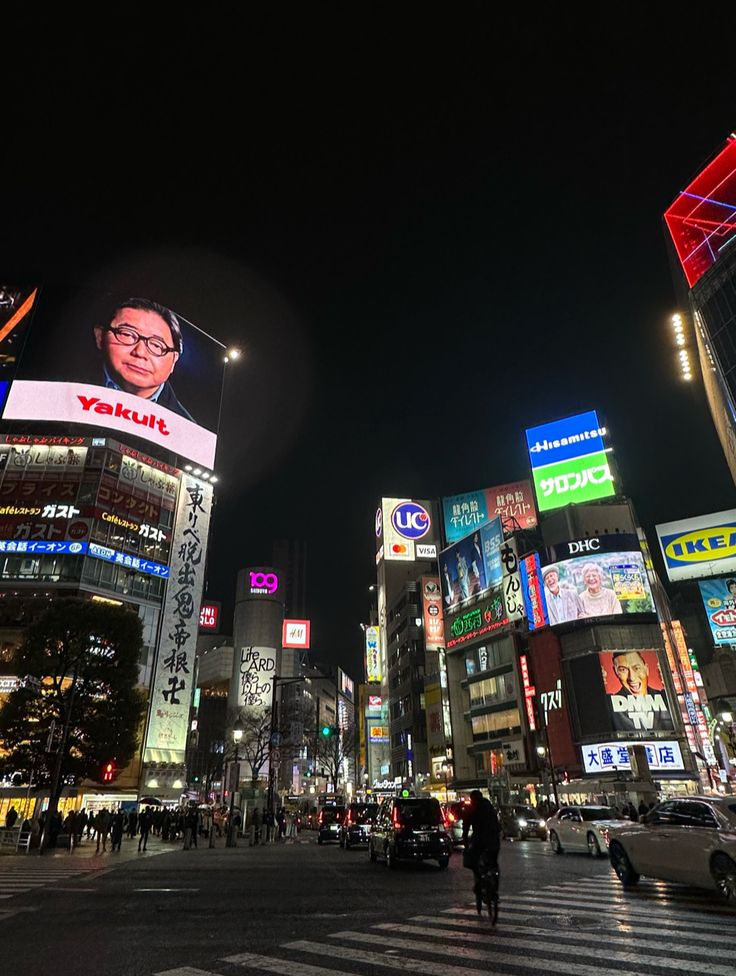 a busy city street at night with tall buildings and billboards lit up in the background