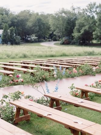 rows of wooden benches with flowers on them in the grass near some trees and bushes