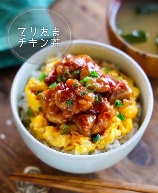 a bowl filled with meat and rice on top of a wooden table next to chopsticks