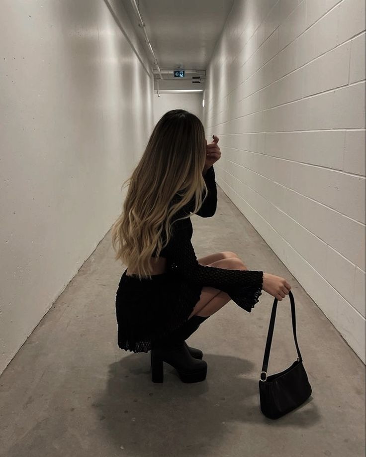 a woman kneeling down in an empty hallway with a handbag on her hip and looking at the camera