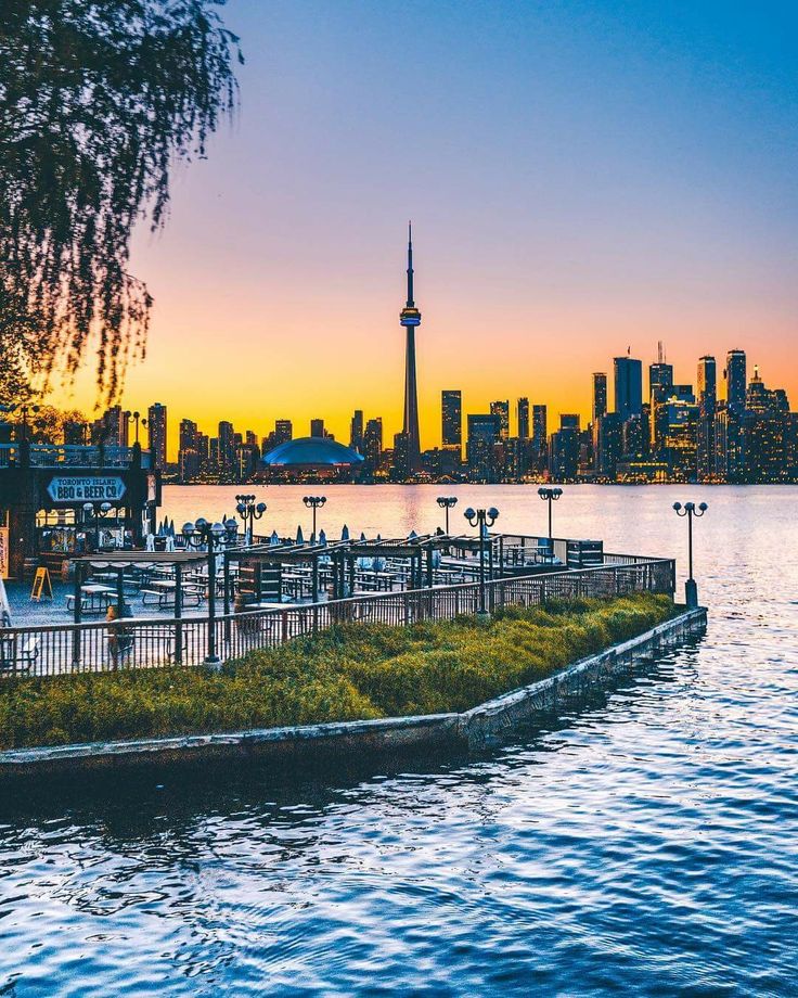 an island with grass growing on it in front of the water and a city skyline