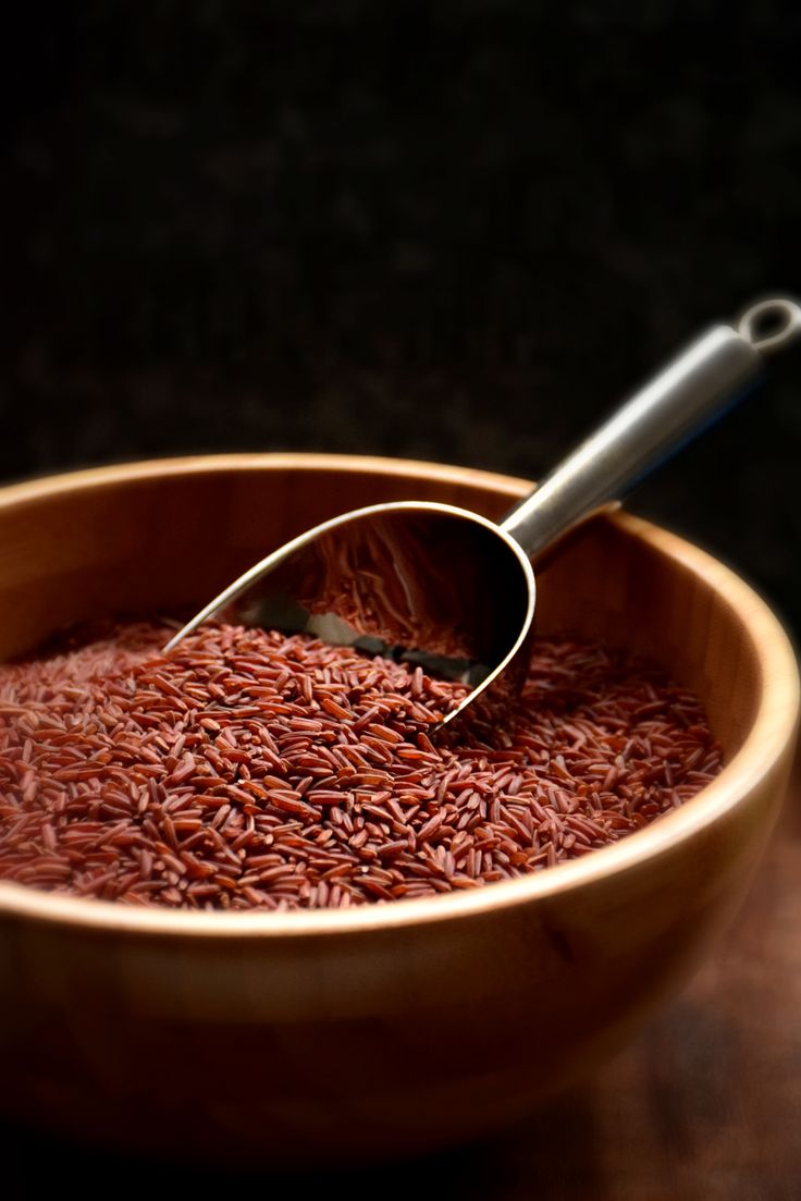 a wooden bowl filled with red rice and a metal spoon in the center, on top of a table