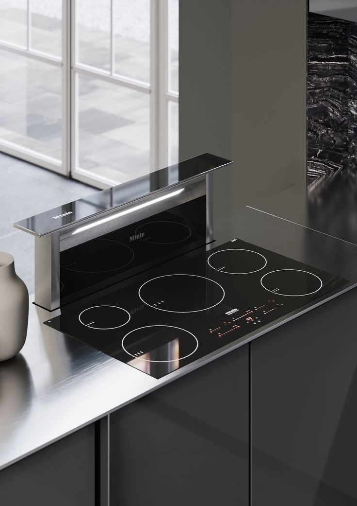 a modern kitchen with stainless steel appliances and black counter tops, along with a white vase