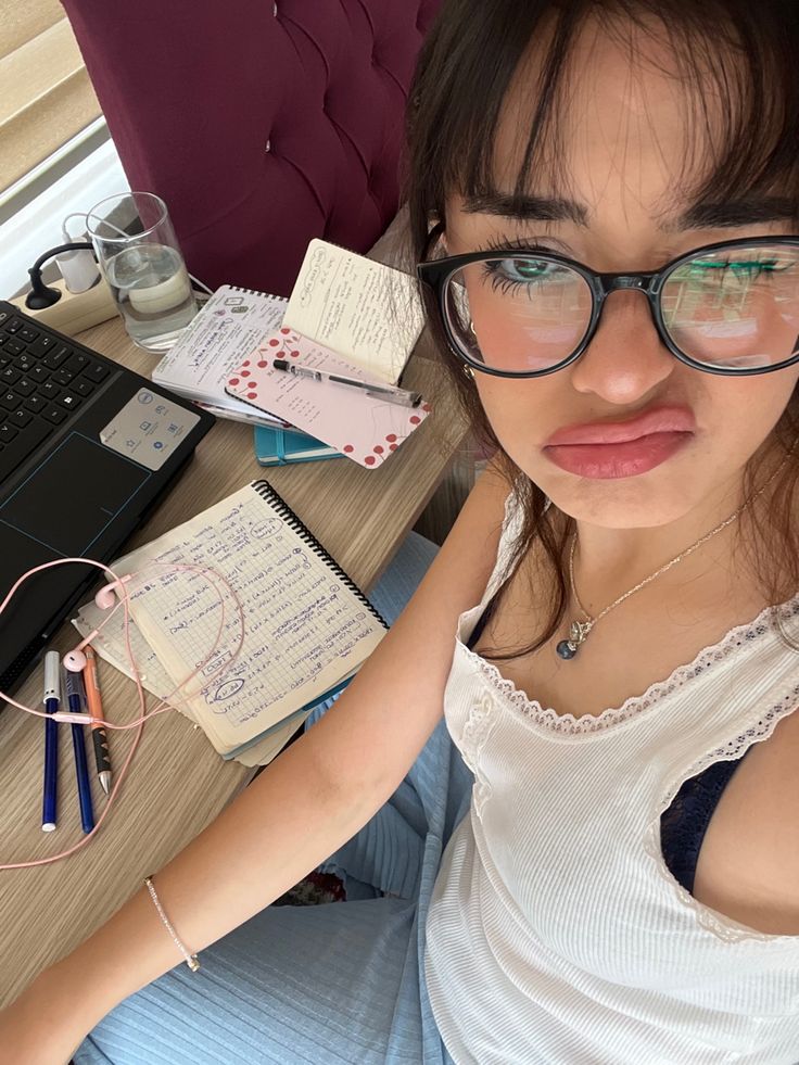 a woman wearing glasses sitting at a desk in front of a laptop computer and notebook