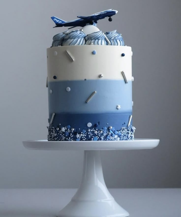 a blue and white cake with an airplane decoration on top is sitting on a pedestal