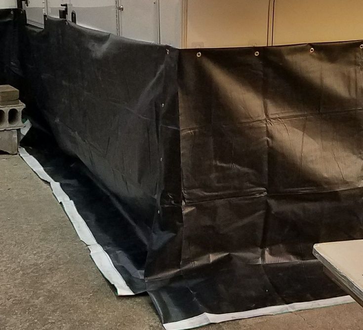 a black tarp covering the back of a white trailer in a storage area next to a wall