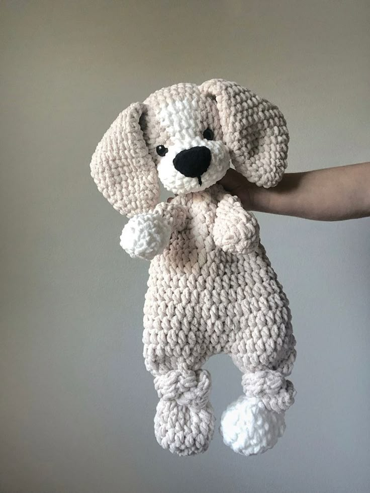 a crocheted stuffed dog is being held up by someone's hand in front of a gray wall