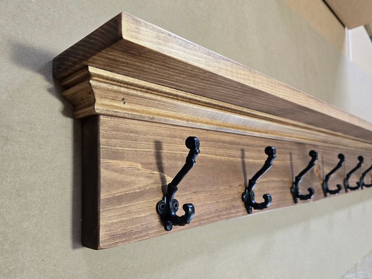 a wooden coat rack with black hooks on the front and back of it, hanging from a wall