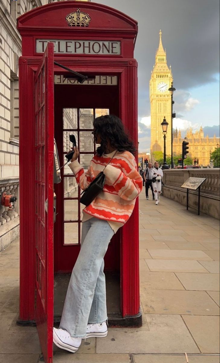 a woman standing in a red phone booth on the side of a street next to a clock tower