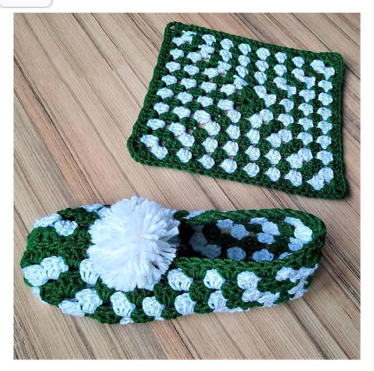 two crocheted slippers with white flowers on them sitting on a wooden floor