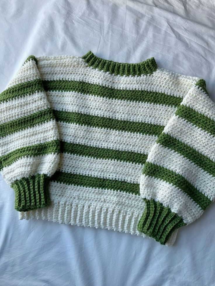 a green and white striped sweater laying on top of a bed next to a pillow