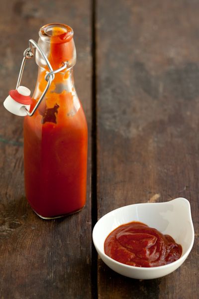 a small white bowl filled with sauce next to a bottle of ketchup on a wooden table