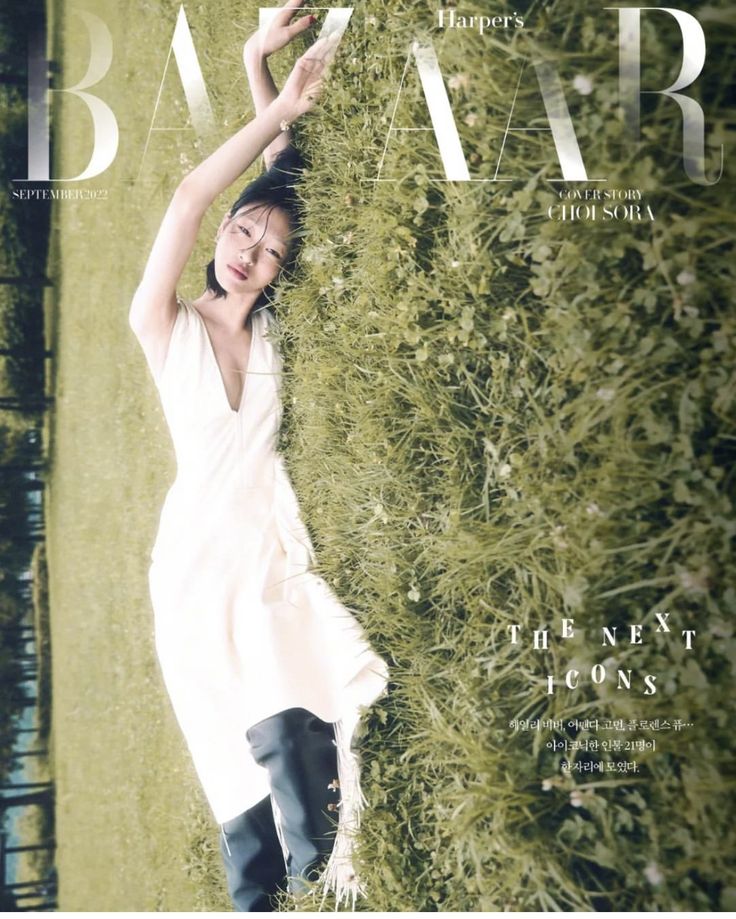 a woman laying on top of a lush green field next to a tall grass covered wall