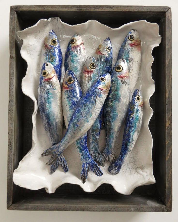 five small fish in a white bowl on a wall mounted plaque with eyeballs and blue paint