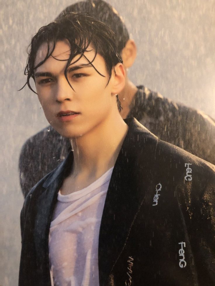 a young man standing in the rain wearing a black jacket and white t - shirt