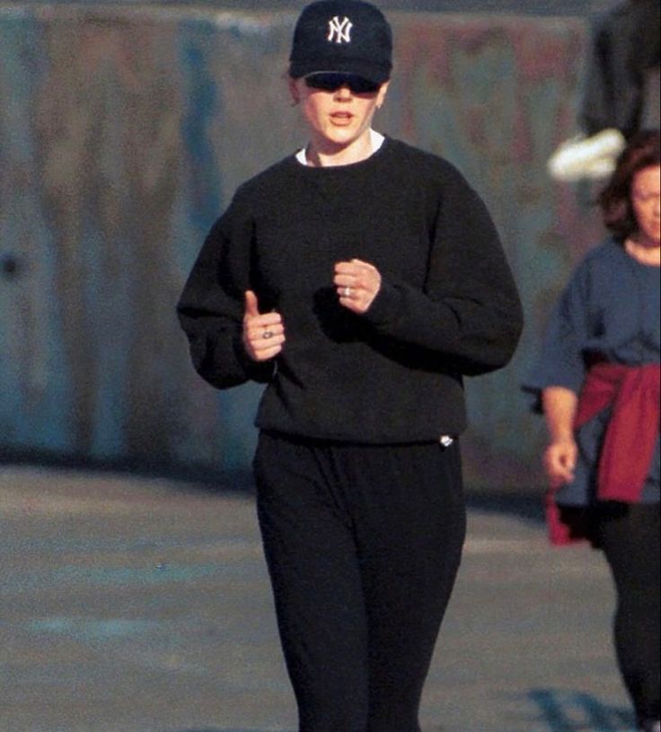 a woman running down the street while wearing a new york yankees hat and black sweatpants