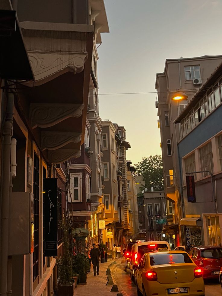 cars parked on the side of a street next to tall buildings and people walking down the sidewalk