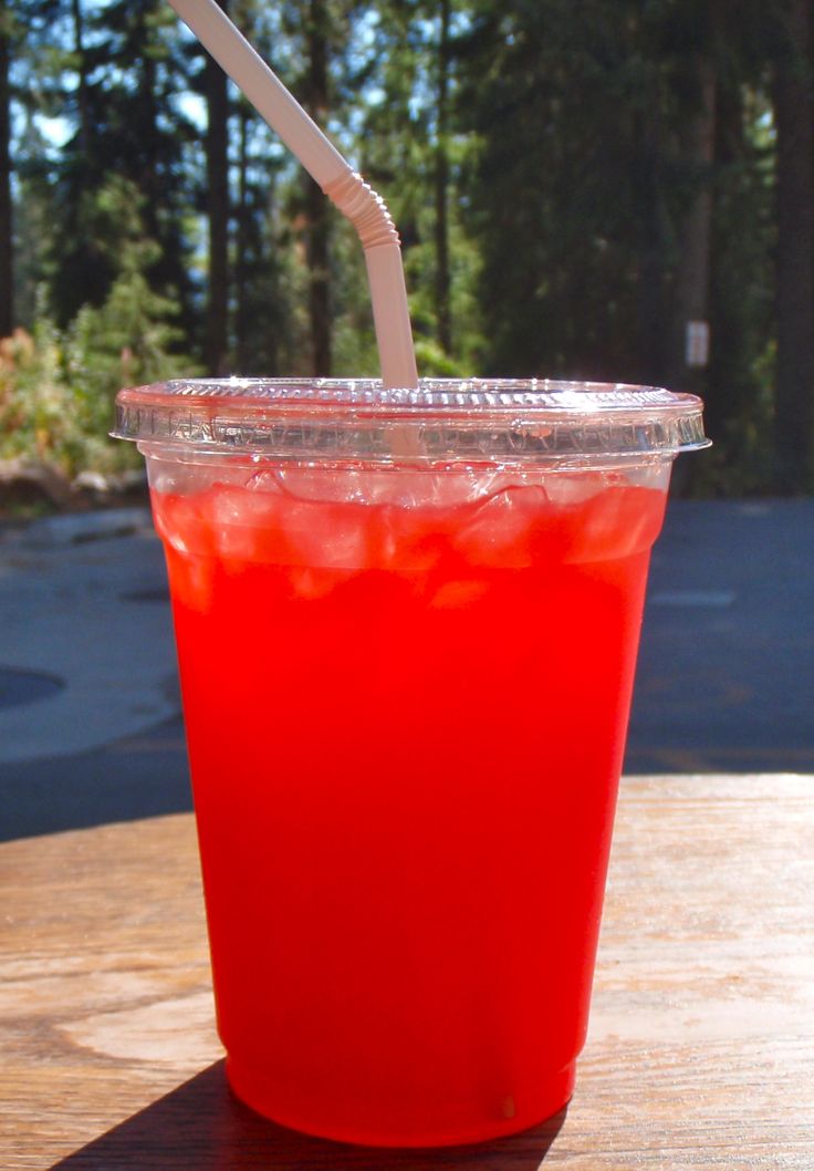 a red drink sitting on top of a wooden table next to a straw in a cup