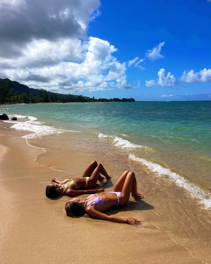 two women laying on the beach in their bathing suits