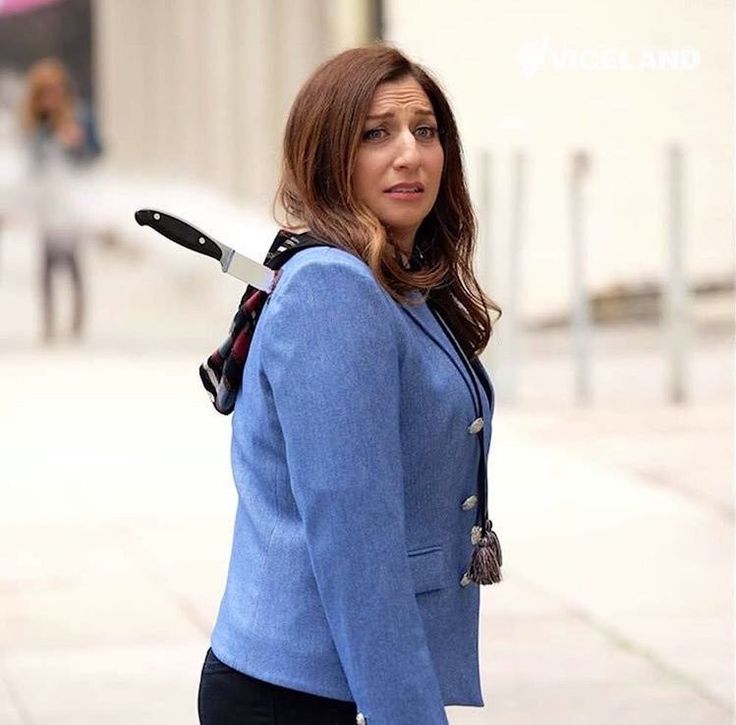 a woman in a blue blazer and black pants is walking down the street with an umbrella on her shoulder