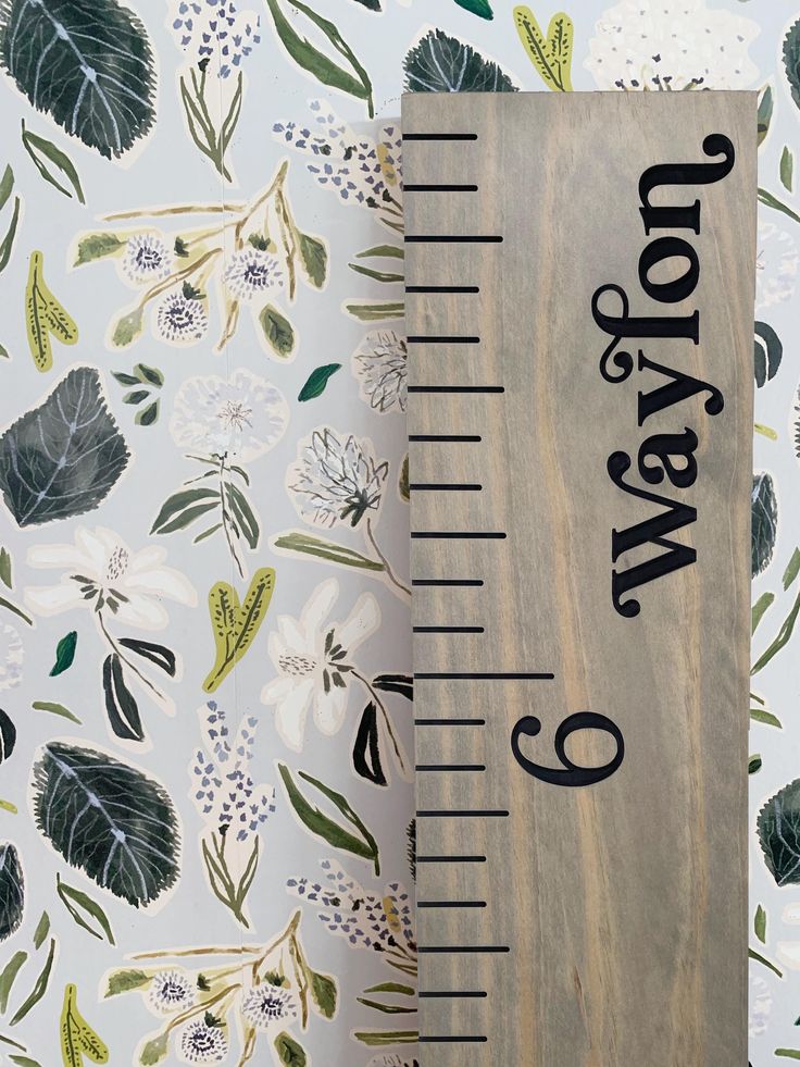 a wooden ruler sitting on top of a table next to a wallpaper covered in leaves