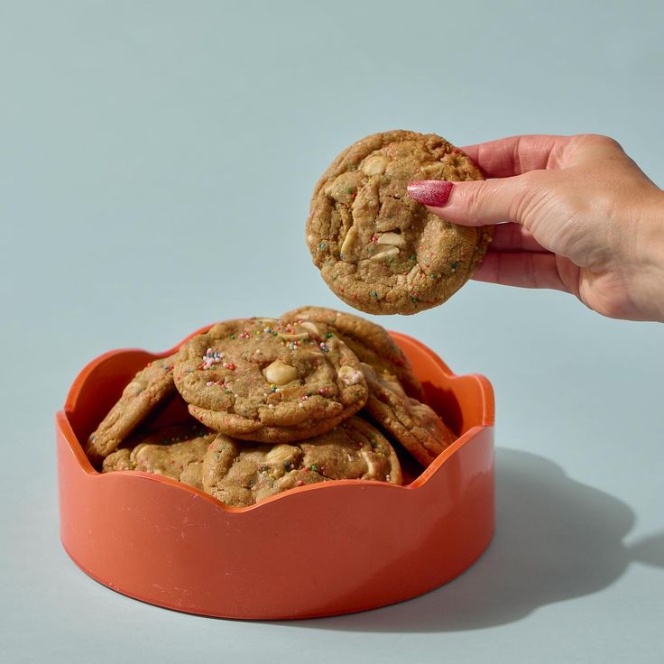 a hand reaching for a cookie in an orange bowl