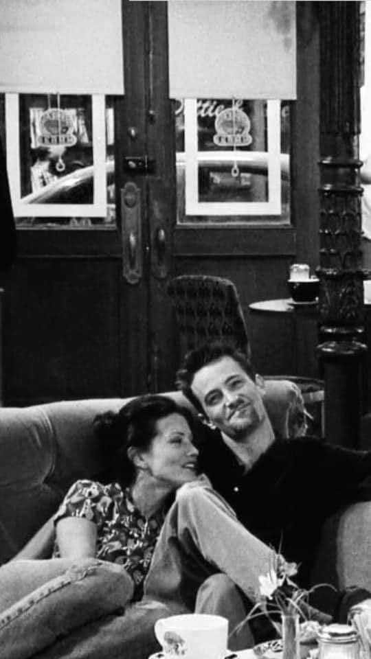 black and white photograph of two people sitting on a couch with coffee cups in front of them