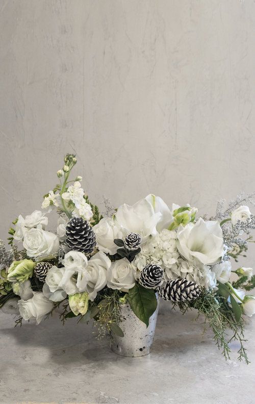 a vase filled with white flowers and pine cones