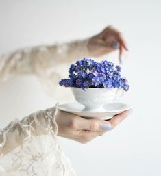 a woman holding a white bowl with blue flowers in it on top of a plate