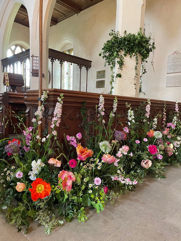 a row of flowers in front of a wooden bench with mirrors on the wall behind it