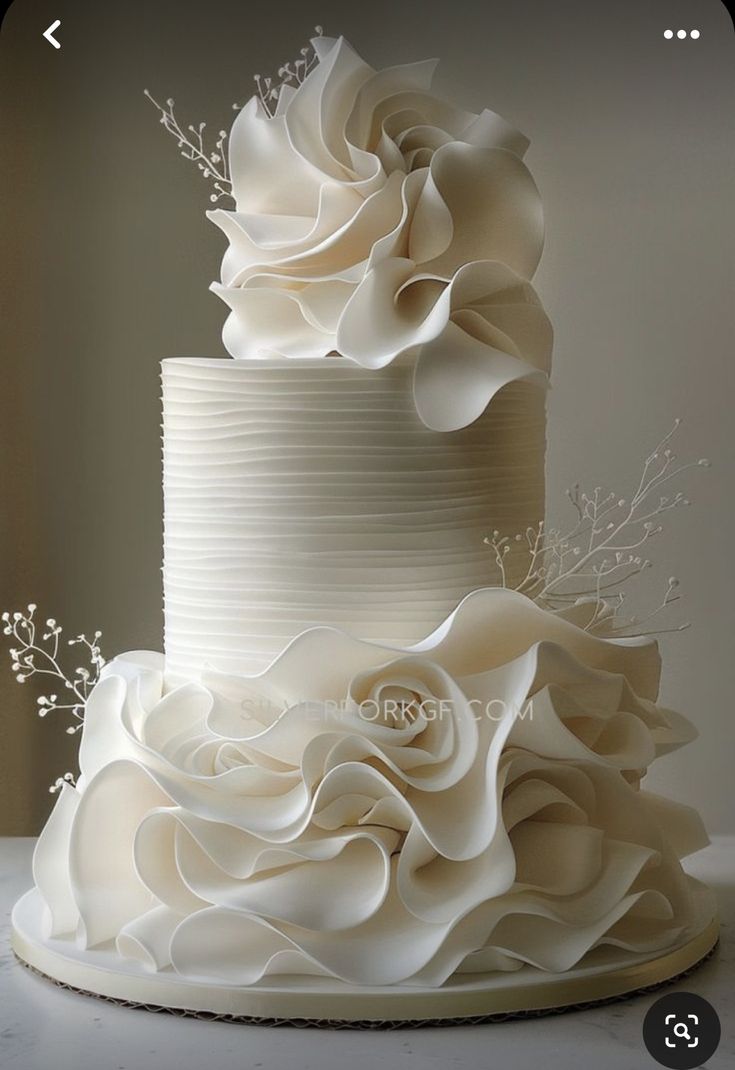 a three tiered white wedding cake with ruffles and flowers on the top