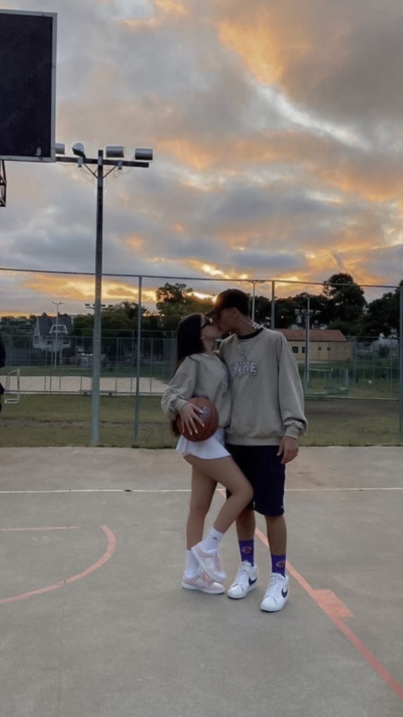 two people standing on a basketball court with the sun setting in the sky behind them