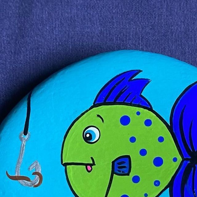 a painted rock with a fish on it and a fishing hook hanging from the side